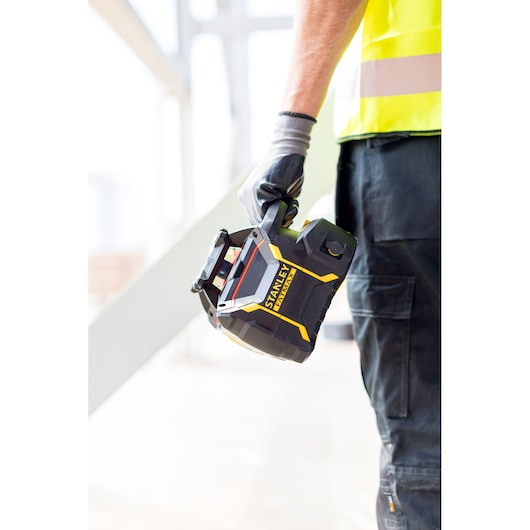 STANLEY FMHT77449-1 laser level in black and yellow, held by a worker wearing gloves and safety vest.