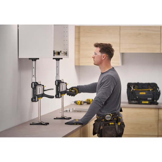 STANLEY FMHT83554-1 cabinet clamp holding wall cabinet during installation, with worker adjusting clamp in kitchen setting.