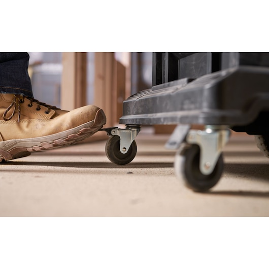 STANLEY FMST1-72363 toolbox caster wheels side view with boot pressing brake lever, workshop setting.