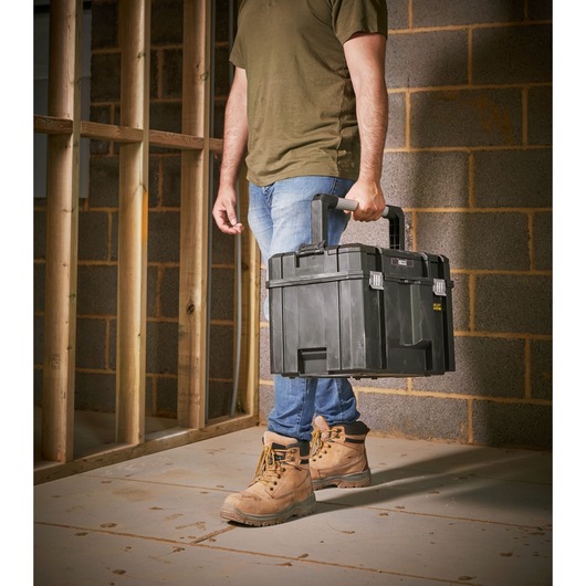 STANLEY FMST1-75796 black toolbox carried by person on construction site, product category photography.