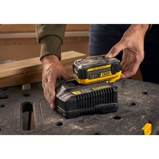 Photo of STANLEY SFMCB14M1 18V lithium-ion battery being placed on charger, shown on a workbench.