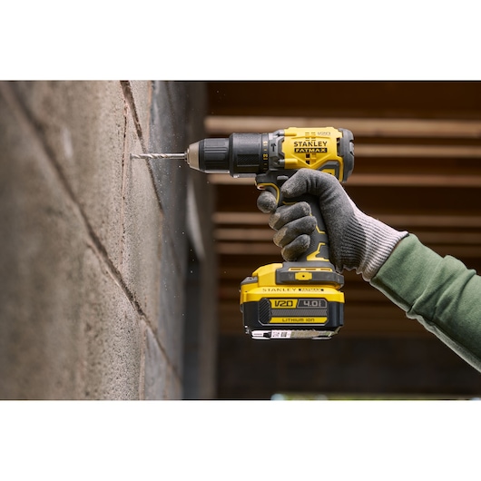 STANLEY SFMCB14M1 cordless drill in use, drilling into concrete wall, close-up view of tool and gloved hand.