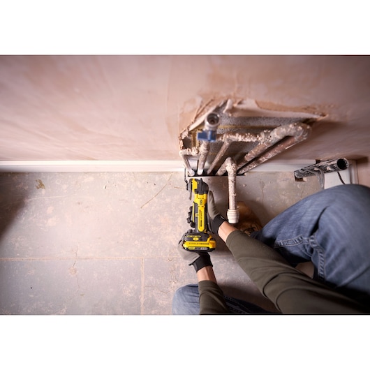 Photo of STANLEY SFMCE510B reciprocating saw used to cut pipes near wall, close-up view.