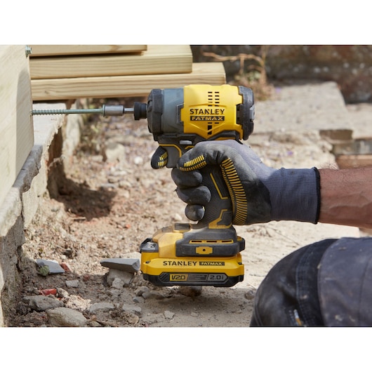 Stanley SFMCF810B impact driver held by gloved hand driving screw into wood, outdoor construction setting.