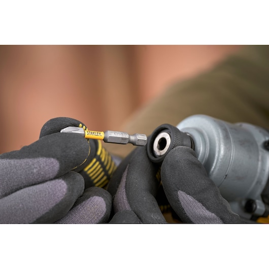 Photo of STANLEY SFMCF830B bit held by gloved hand near drill chuck, close-up product view.