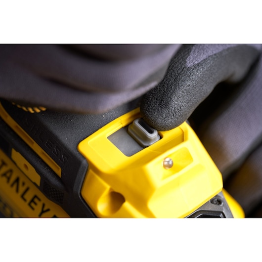 Photo of STANLEY SFMCF940M1 cordless tool close-up with gloved hand pressing gray button, yellow and black body.