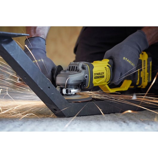 STANLEY SFMCG400B angle grinder in use cutting metal, yellow and black tool with visible sparks.