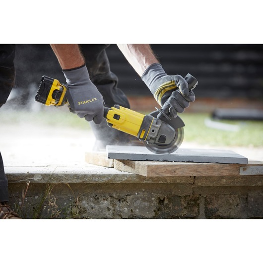 STANLEY SFMCG400B cordless angle grinder in use cutting a concrete slab outdoors.