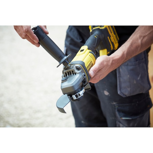 Photo of STANLEY SFMCG400B cordless angle grinder being held and assembled by a person in workwear.