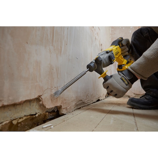 Photo of STANLEY SFMCH900B rotary hammer in use, chiseling plaster on a wall near the floor.