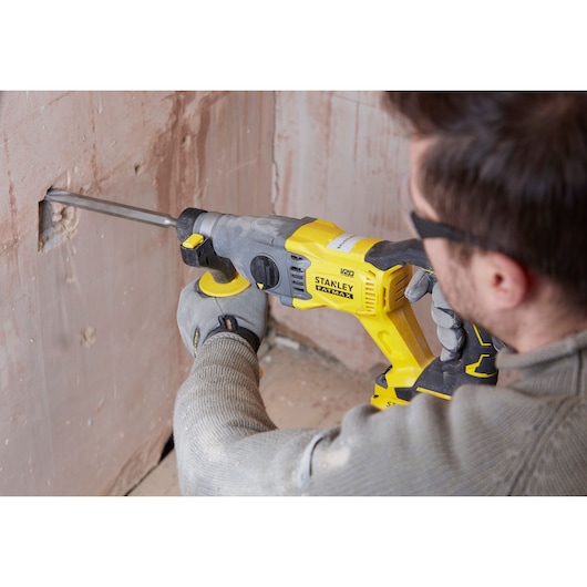 Photo of STANLEY SFMCH900M22 rotary hammer drilling into plaster wall, side view, yellow and black tool.