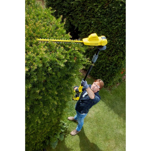 Photo of a person using STANLEY SFMCPH845M1 pole hedge trimmer to trim tall bushes outdoors.