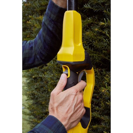 Close-up photo of hands holding a STANLEY SFMCPH845M1 hedge trimmer handle near shrubbery.