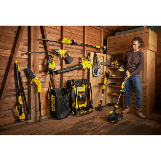 STANLEY SFMCPH845M1 corded and cordless garden tools set in shed, person holding string trimmer.