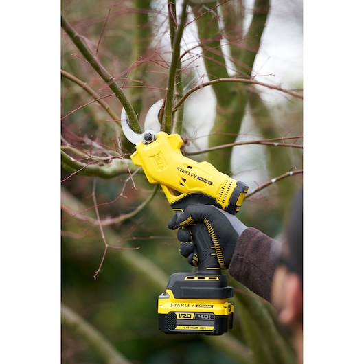Stanley SFMCPP32M1 cordless pruner cutting tree branches, yellow and black design, close-up outdoors.