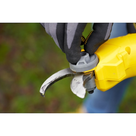 STANLEY SFMCPP32M1 yellow pruner close-up with gloved hand adjusting gray dial outdoors.