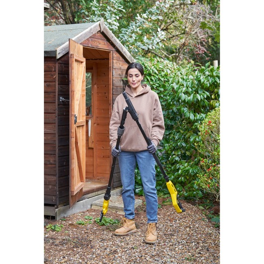 Photography of STANLEY SFMCPP632D1 pole saw held outdoors by person in garden near wooden shed.
