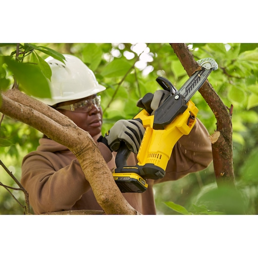 STANLEY SFMCPS415D1 cordless pruning saw cutting a tree branch outdoors, operator wearing gloves.