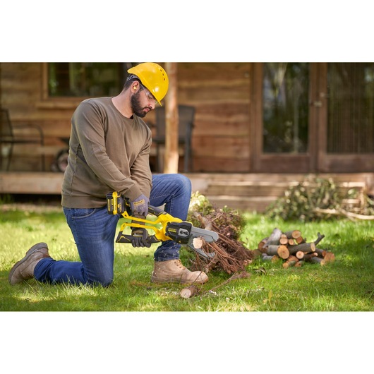 Photo of a person using a STANLEY SFMCPS515B cordless chainsaw to cut branches outdoors on grass.