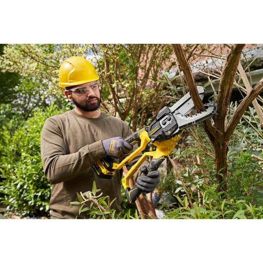 Photo of worker using STANLEY SFMCPS515M1 cordless chainsaw to cut tree branches in garden.