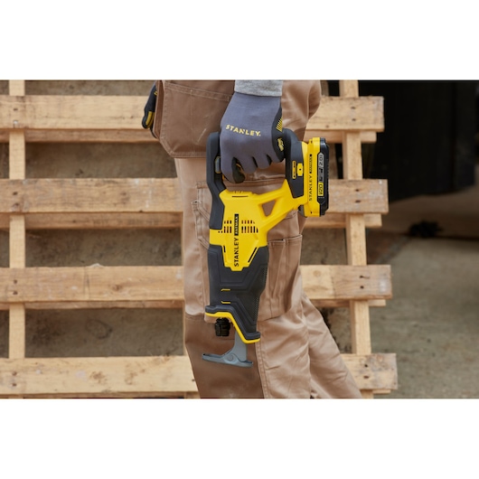 STANLEY SFMCS300B reciprocating saw held by a gloved hand, yellow and black design, construction setting.