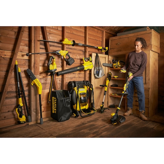STANLEY SFMCST933B garden tools displayed in wooden shed, one person holding a string trimmer.