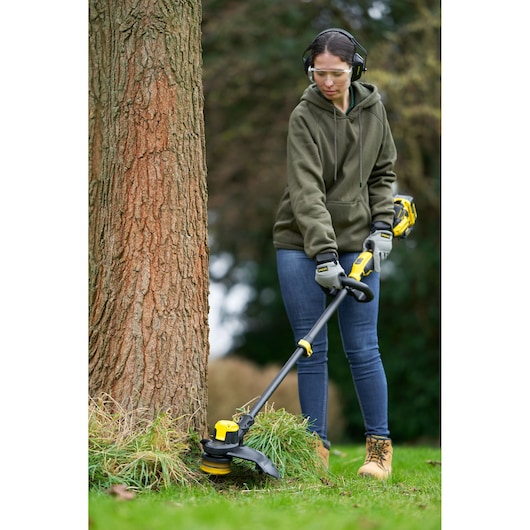 STANLEY SFMCSTB933M cordless string trimmer, yellow and black, used outdoors near tree.