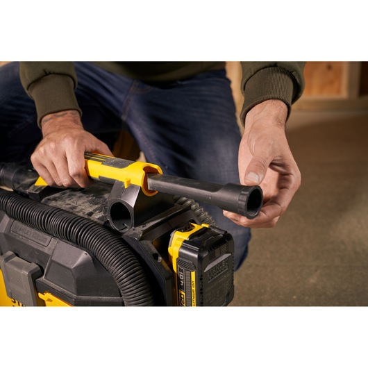 Photo of hands attaching hose to STANLEY SFMCV002B vacuum cleaner, close-up view of connector and battery.