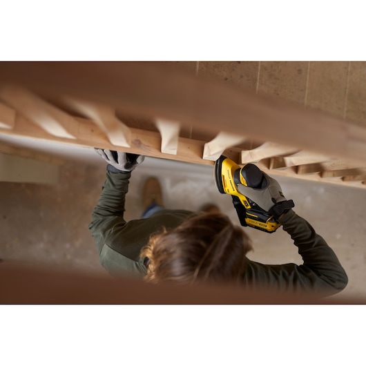 Photo of person using STANLEY SFMCW221B cordless sander on wooden staircase railing.
