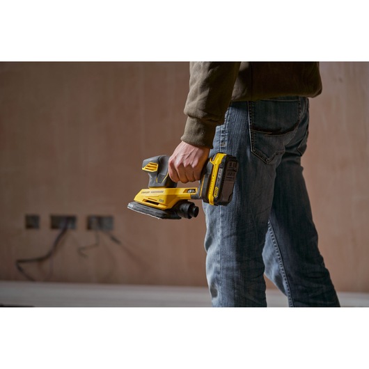 Person holding STANLEY SFMCW221D1S cordless sander, yellow and black, shown in use, product photography.