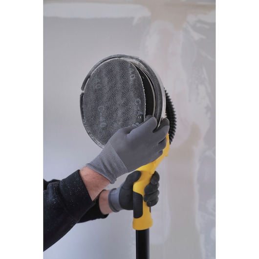 STANLEY SFMEE500S drywall sander close-up, gloved hands adjusting round sanding pad, indoor setting.