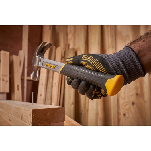 STANLEY STHT0-51309 claw hammer held by gloved hand, near nail and wood, workshop background.