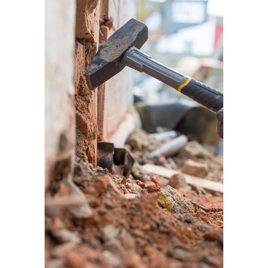 STANLEY STHT0-51910 hammer breaking brick wall, close-up on construction site.