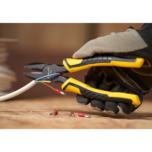 Photo of STANLEY STHT0-74454 combination pliers with yellow and black handle cutting electrical wires, held by gloved hand.