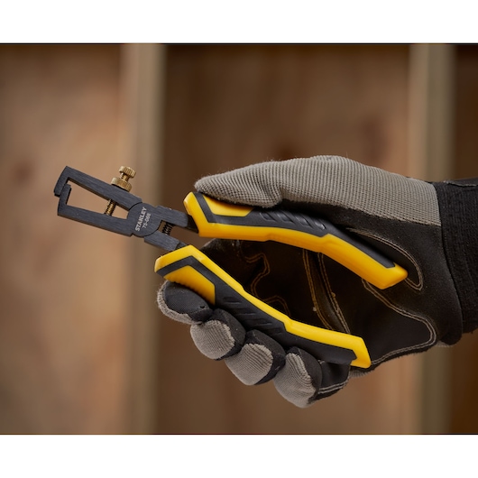 STANLEY STHT0-75068 wire stripper pliers with yellow and black handles, side angle, held by gloved hand.