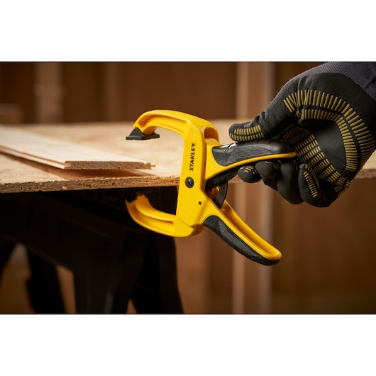 STANLEY STHT0-83199 trigger clamp holding wood, side angle, yellow grip tool in hand.
