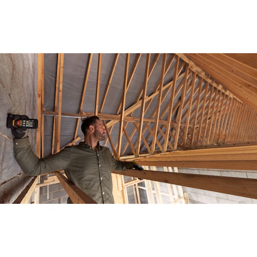 Person using STANLEY STHT1-77140 laser distance measurer inside wooden roof construction.