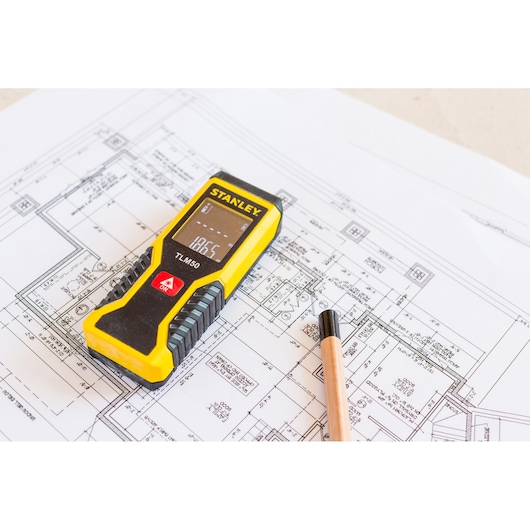 STANLEY STHT1-77409 laser distance meter on architectural blueprint with pencil, angled top view.