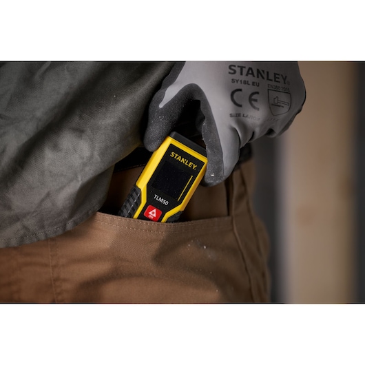 STANLEY STHT1-77409 laser distance measurer TLM50 being placed in a pants pocket by a gloved hand.