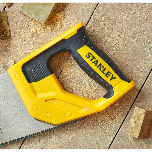 STANLEY STHT20349-1 hand saw with yellow and black handle, close-up on wooden surface with sawdust.