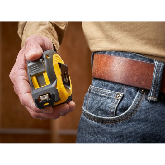 STANLEY STHT37233 tape measure with yellow and black casing held next to a denim pocket and brown leather belt.