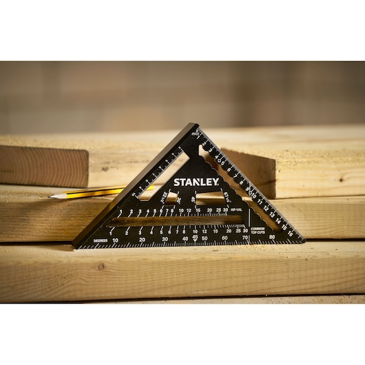 STANLEY STHT46101-0 black triangular carpenter’s square on stacked wood, pencil in background.