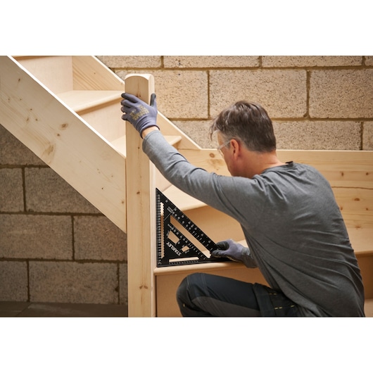 Photo of STANLEY STHT46102-0 black carpenter square used on wooden stairs, person measuring.