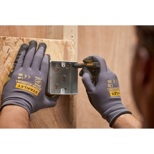 Hands with STANLEY gloves mark a metal box on wood using a STANLEY pencil during construction.