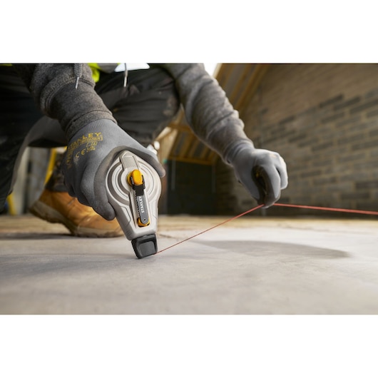 Photo of STANLEY STHT47611-0 chalk line reel in use on construction site floor, worker wearing gloves.