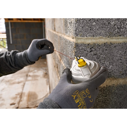 STANLEY STHT47611-0 chalk line tool held by gloved hand against a masonry wall, close-up photography.
