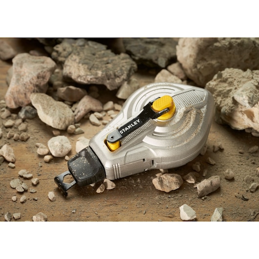 STANLEY STHT47611-0 silver chalk line reel with yellow accents on rocky ground.