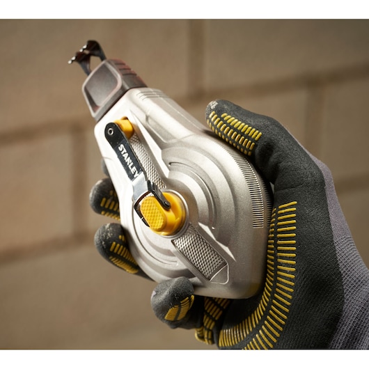 STANLEY STHT47611-0 chalk reel held in gloved hand, silver body, yellow accents, close-up photo.