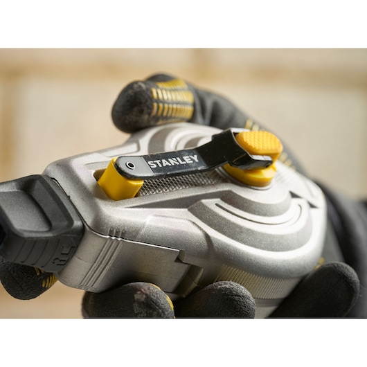 Stanley STHT47611-0 tape measure close-up, silver and yellow design, held by gloved hand.