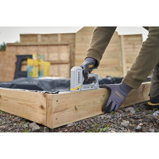 STANLEY STHT70150-0 staple gun in use, fastening plastic to wooden frame outdoors.